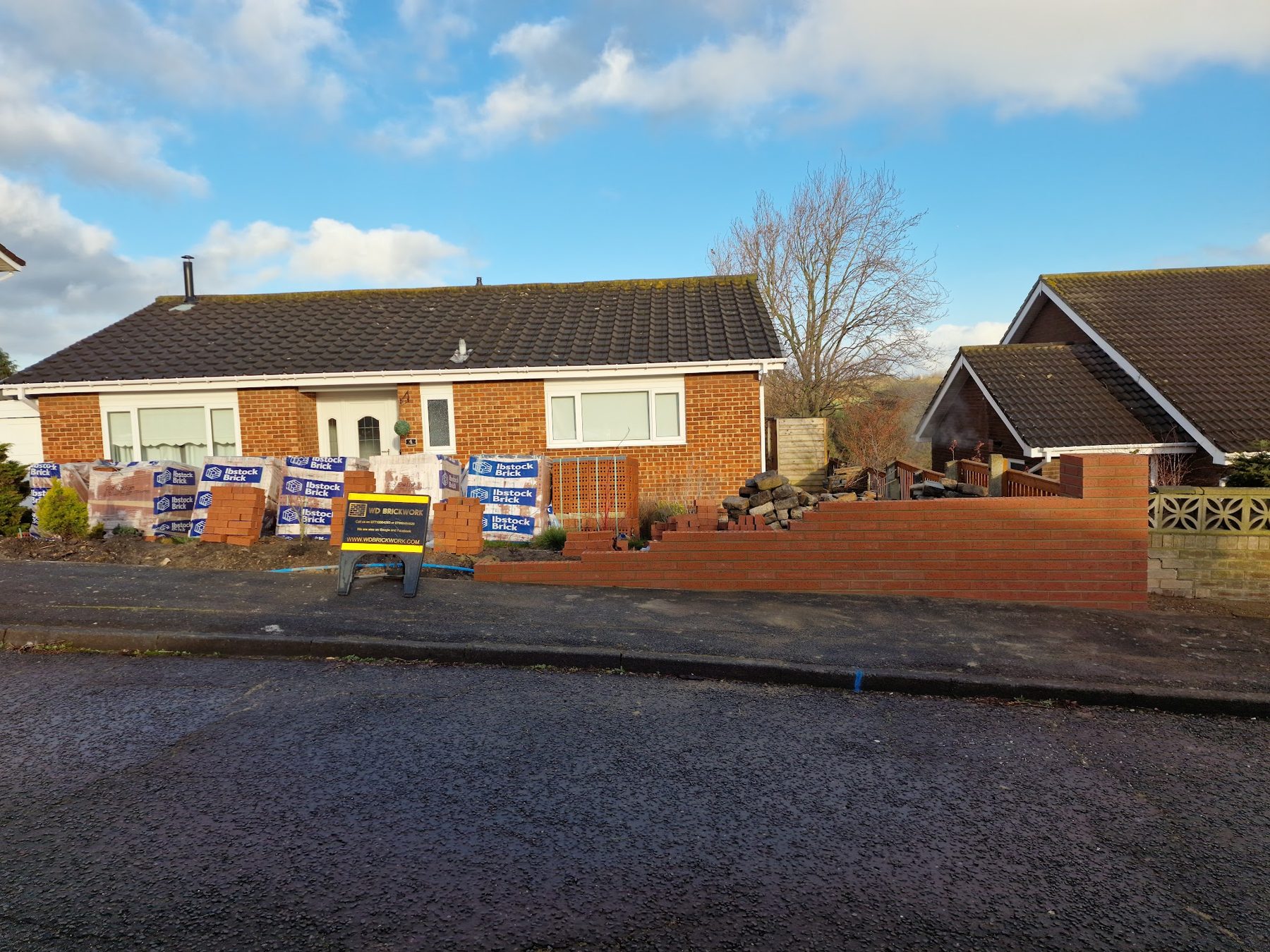 A bungalow with a new low brick front wall, bricks palleted ready on the drive