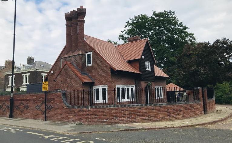 A finished red brick house on a corner plot with a patterned boundary wall