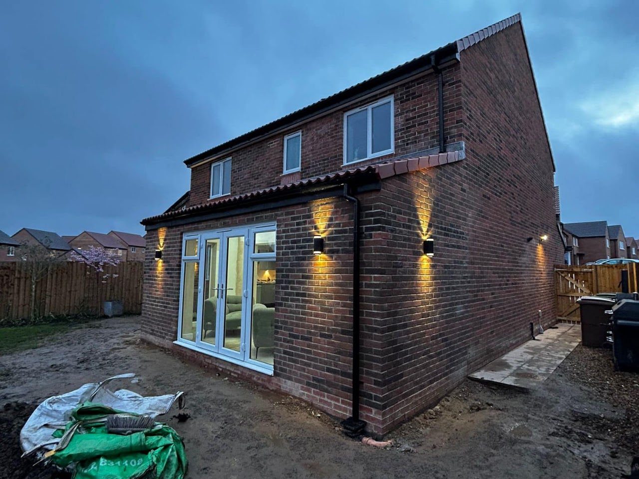 A finished rear extension at dusk, wall lights on beside French doors